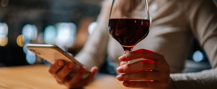 Woman holding a glass of wine and a smartphone at a bar