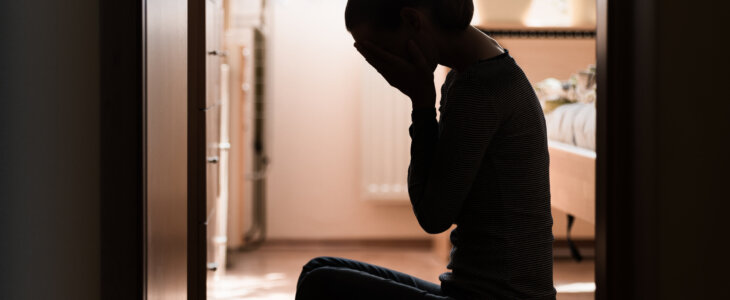 Sad young woman sitting on room floor crying with hand over face